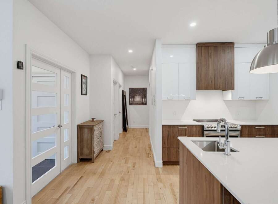 Step into a modern and inviting home featuring a sleek kitchen with white and wood cabinetry, a spacious island with a sink, and stainless steel appliances.