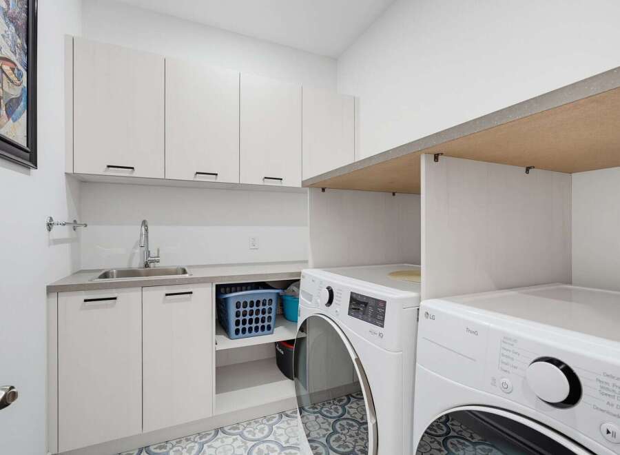This modern laundry room features sleek white cabinetry, a stainless steel sink, and a convenient countertop space.