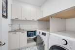 This modern laundry room features sleek white cabinetry, a stainless steel sink, and a convenient countertop space.