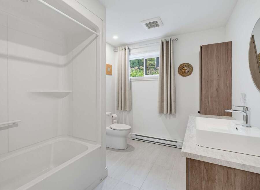 This modern bathroom features a pristine white bathtub and shower combo, perfect for relaxing soaks.