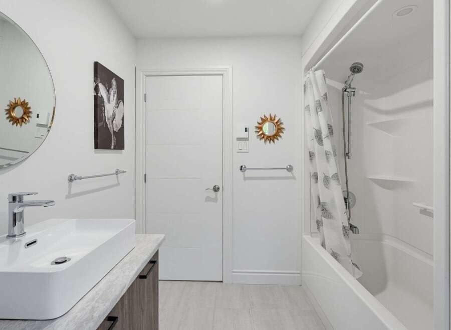 This modern bathroom features a sleek vessel sink atop a vanity with ample storage, complemented by a large round mirror and a striking black and white wall art.