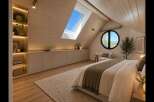 Experience modern attic living in this beautifully designed bedroom, featuring a sloped wooden ceiling and a large skylight that floods the space with natural light.