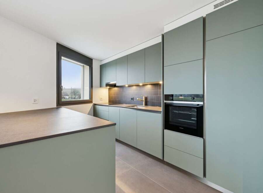 Discover this modern kitchen featuring sleek, sage green cabinetry and a spacious island with a stone countertop.