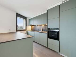 Discover this modern kitchen featuring sleek, sage green cabinetry and a spacious island with a stone countertop.