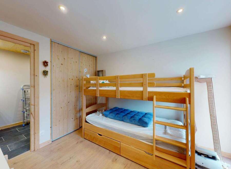 This charming bedroom features a space-saving wooden bunk bed with an integrated pull-out drawer, perfect for maximizing room utility.