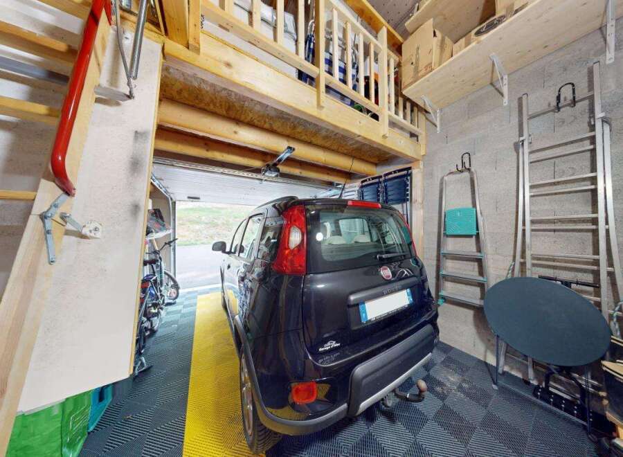 Discover this spacious garage featuring a convenient loft storage area accessible by a sturdy wooden staircase.