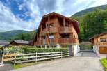 Experience alpine living in this charming wooden chalet, nestled against a backdrop of lush green mountains.