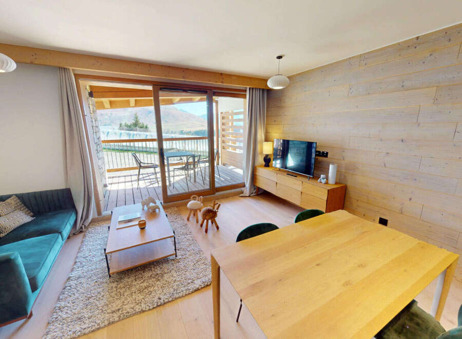 Experience modern mountain living in this beautifully appointed apartment, featuring a plush teal sectional sofa and a warm, wood-paneled accent wall.