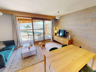 Experience modern mountain living in this beautifully appointed apartment, featuring a plush teal sectional sofa and a warm, wood-paneled accent wall.