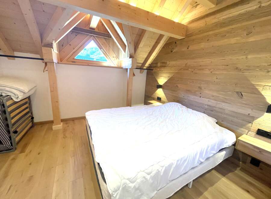 Experience rustic charm in this attic bedroom, featuring a cozy bed with crisp white linens and a unique triangular window offering scenic views.