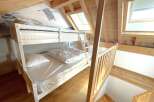 Discover this charming attic bedroom featuring a white bunk bed with comfortable mattresses and pillows, perfect for families or guests.