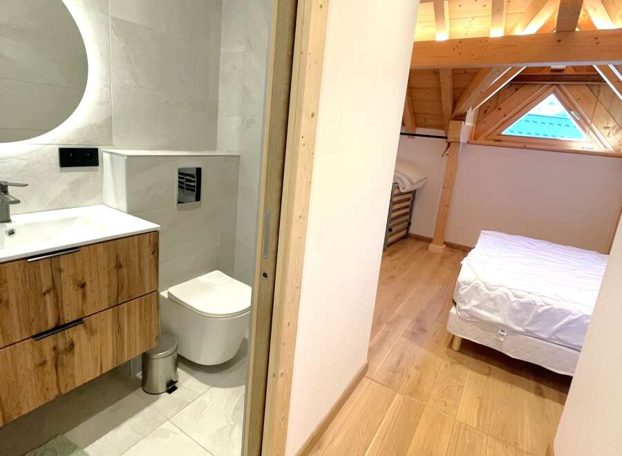 Discover this charming property featuring a modern bathroom with a sleek vanity and toilet, complemented by a spacious bedroom with a cozy bed and exposed wooden beams.