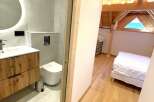 Discover this charming property featuring a modern bathroom with a sleek vanity and toilet, complemented by a spacious bedroom with a cozy bed and exposed wooden beams.
