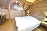 Experience rustic charm in this attic bedroom, featuring a cozy bed with crisp white linens and a unique triangular window offering scenic views.