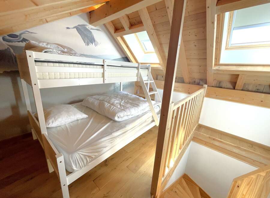 Discover this charming attic bedroom featuring a white bunk bed with comfortable mattresses and pillows, perfect for families or guests.