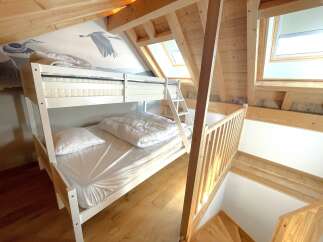 Discover this charming attic bedroom featuring a white bunk bed with comfortable mattresses and pillows, perfect for families or guests.