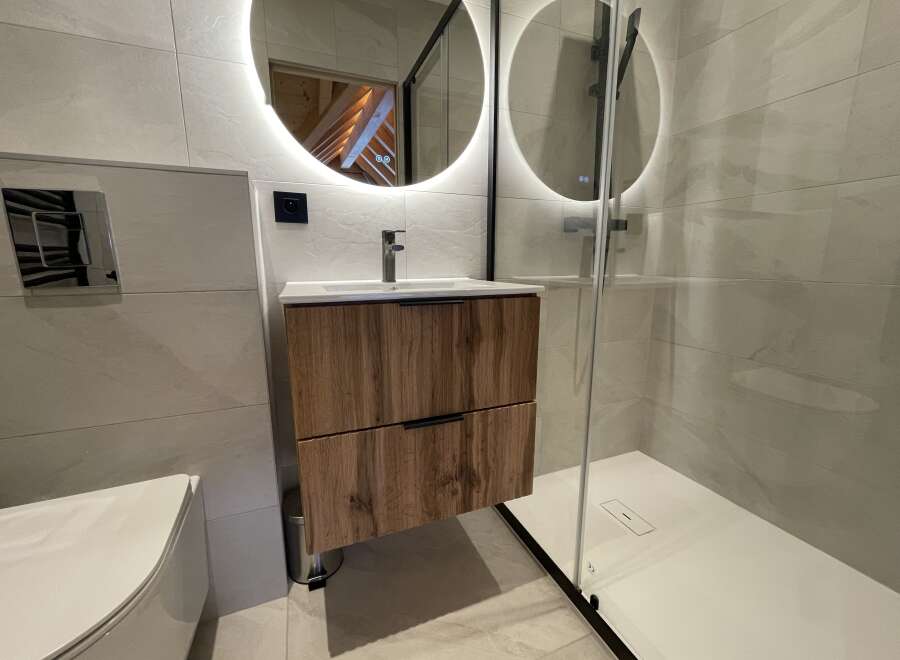 Experience modern luxury in this stunning bathroom featuring a floating wood vanity with sleek black hardware.