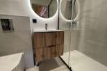 Experience modern luxury in this stunning bathroom featuring a floating wood vanity with sleek black hardware.