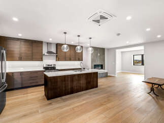 Experience modern living in this stunning kitchen and living area, featuring sleek dark wood cabinetry, a spacious island with a waterfall countertop, and a contemporary gas fireplace.