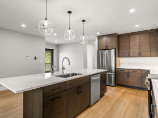 Experience modern living in this stunning kitchen featuring sleek dark wood cabinetry and a spacious quartz island with a waterfall edge.
