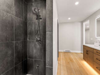 Experience modern luxury in this stunning bathroom featuring a spacious walk-in shower with sleek, dark tilework and a contemporary showerhead.