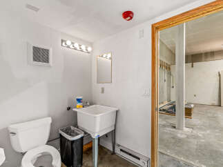 This functional bathroom space features a white toilet, a utility sink, and a vanity with a mirror and bright lighting.