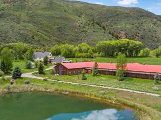 Experience serene country living with this picturesque property featuring a charming yellow farmhouse and a long, rustic barn with a vibrant red roof.