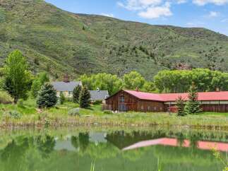 Discover this picturesque property featuring a charming yellow house and a rustic wooden barn with a vibrant red roof, all set against a stunning mountain backdrop.