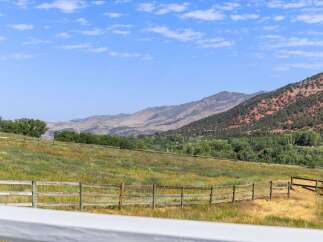 Experience the beauty of this expansive property, featuring rolling green hills dotted with wildflowers and a rustic wooden fence.