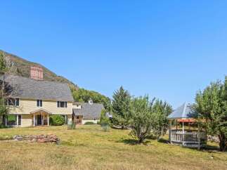 Nestled against a scenic mountain backdrop, this charming property features a spacious yellow house with a prominent brick chimney and a welcoming front porch.