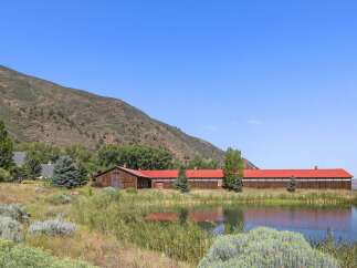 Discover this expansive property featuring a long, rustic wooden barn with a vibrant red roof, nestled beside a tranquil pond.