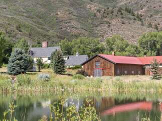 Nestled against a scenic mountain backdrop, this property features a charming yellow house with a brick chimney and a spacious red-roofed barn.