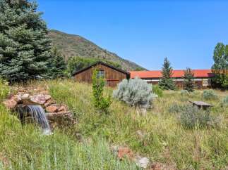 Discover this charming property featuring a rustic wooden building with a vibrant red roof, nestled amidst lush greenery and mature trees.
