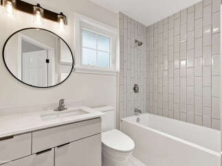 This modern bathroom features a sleek vanity with ample storage, a stylish oval mirror, and a bright window.