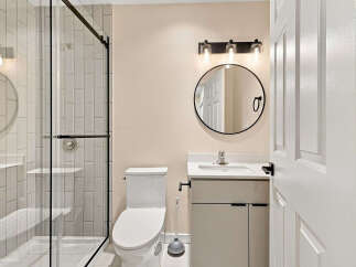 This modern bathroom features a sleek glass-enclosed shower with subway tile and a chrome handle.