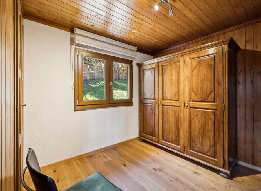 Experience rustic charm in this cozy room featuring a large wooden wardrobe and a charming window overlooking a lush green yard.