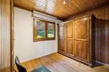 Experience rustic charm in this cozy room featuring a large wooden wardrobe and a charming window overlooking a lush green yard.