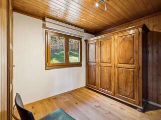 Experience rustic charm in this cozy room featuring a large wooden wardrobe and a charming window overlooking a lush green yard.