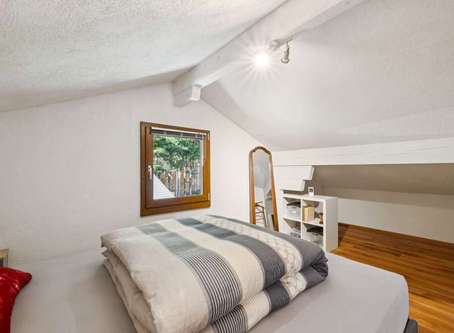 Discover this charming attic bedroom, featuring a cozy bed with a stylish striped comforter and a large window offering picturesque views of the outdoors.