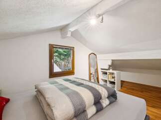 Discover this charming attic bedroom, featuring a cozy bed with a stylish striped comforter and a large window offering picturesque views of the outdoors.