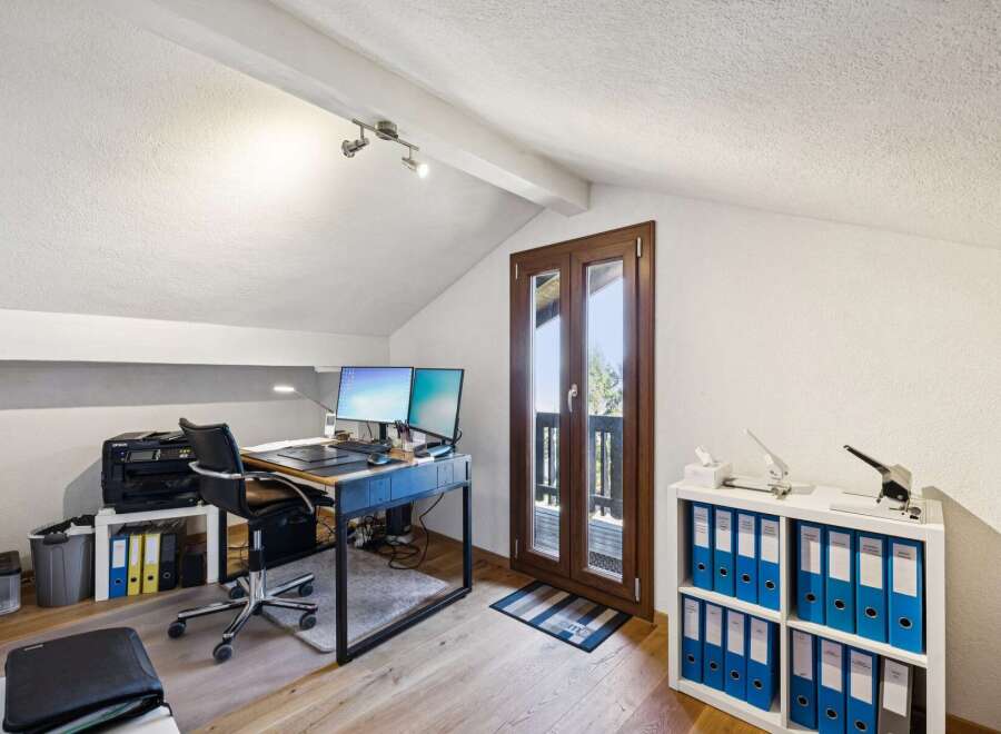 This attic home office features a spacious desk with dual monitors, a comfortable ergonomic chair, and ample storage with a printer and filing cabinets.