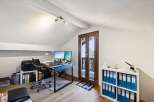 This attic home office features a spacious desk with dual monitors, a comfortable ergonomic chair, and ample storage with a printer and filing cabinets.
