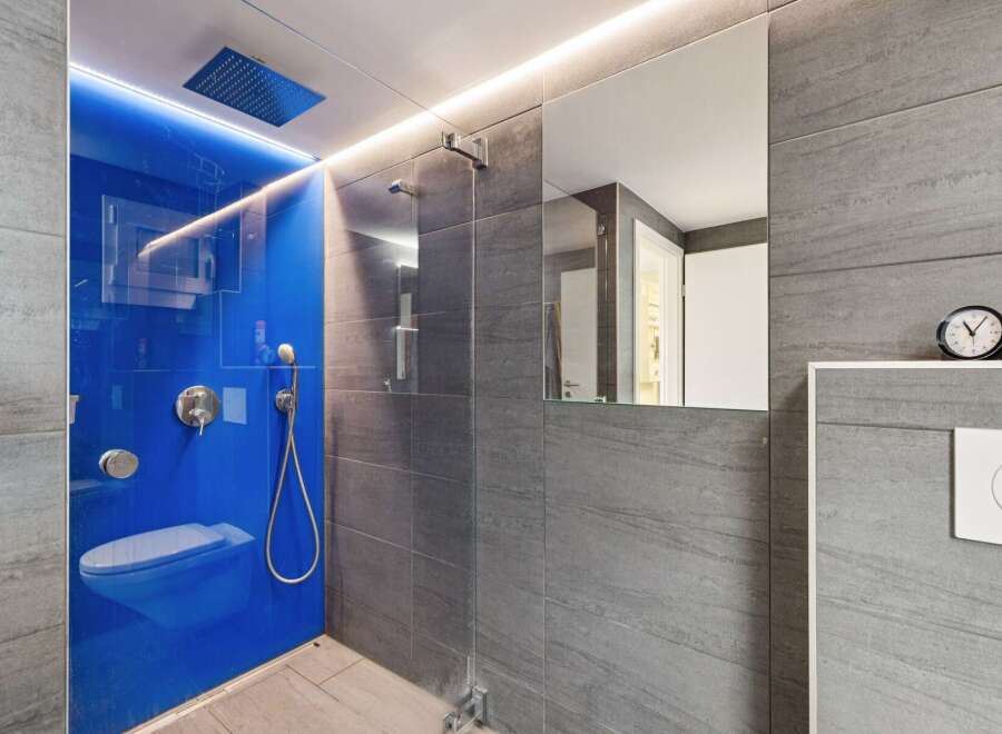 Experience modern luxury in this stunning bathroom featuring a vibrant blue glass shower enclosure with integrated LED lighting.
