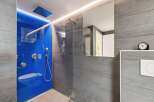Experience modern luxury in this stunning bathroom featuring a vibrant blue glass shower enclosure with integrated LED lighting.