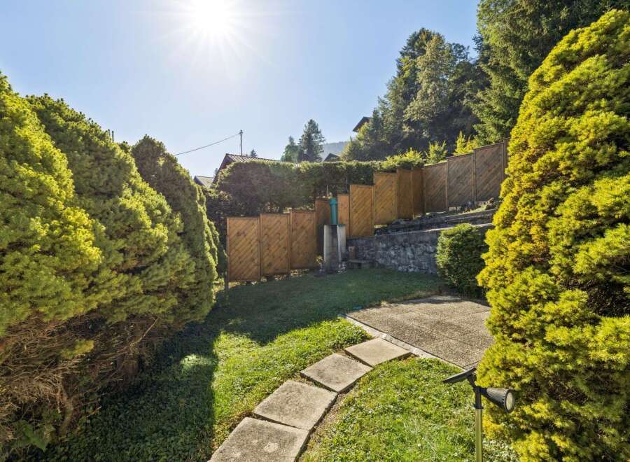 Enjoy the sunshine in this beautifully landscaped backyard, featuring lush green trees and a charming stone pathway leading through the garden.