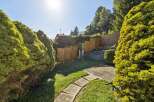 Enjoy the sunshine in this beautifully landscaped backyard, featuring lush green trees and a charming stone pathway leading through the garden.