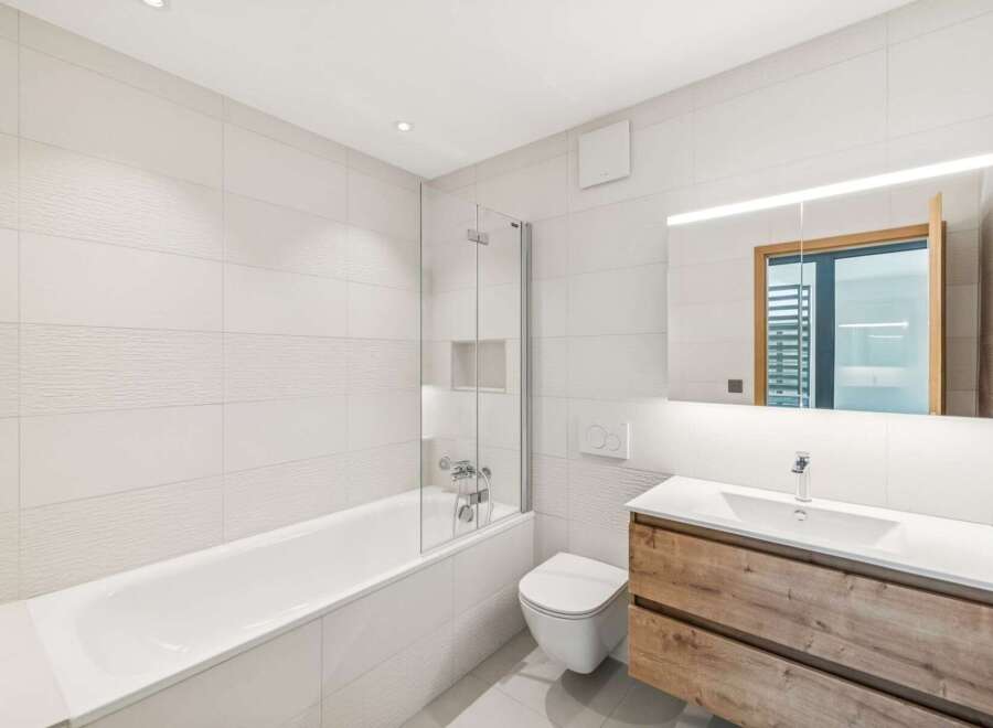 Experience modern comfort in this beautifully appointed bathroom, featuring a sleek bathtub with a glass shower screen and a wall-mounted toilet.