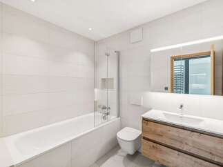 Experience modern comfort in this beautifully appointed bathroom, featuring a sleek bathtub with a glass shower screen and a wall-mounted toilet.