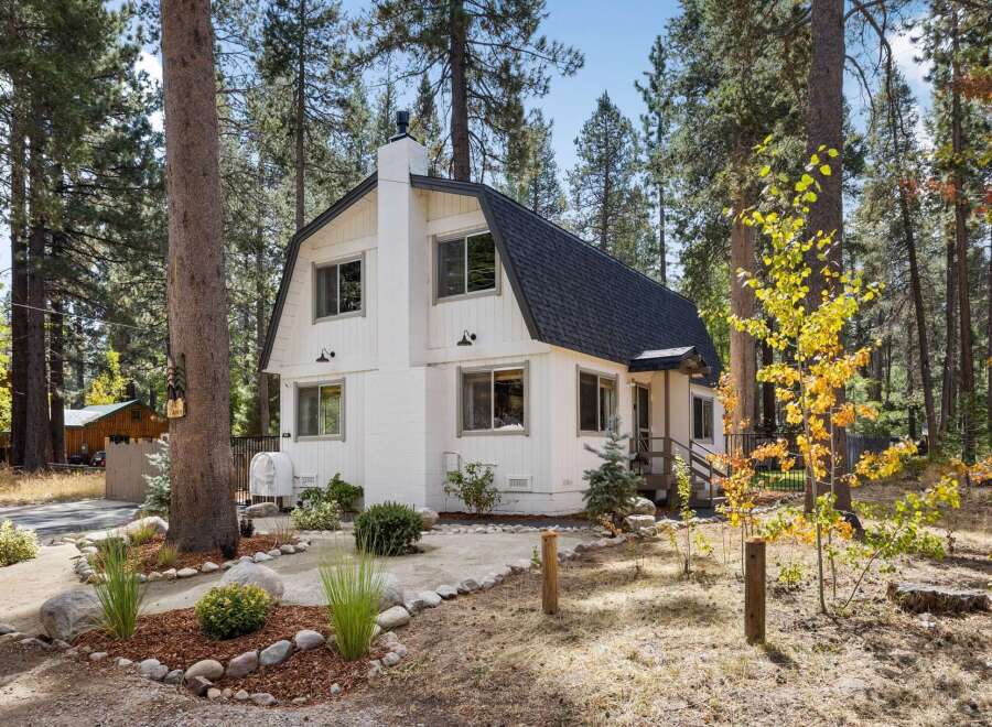 Charming white A-frame home nestled among tall pine trees, offering a serene mountain retreat.