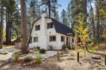 Charming white A-frame home nestled among tall pine trees, offering a serene mountain retreat.